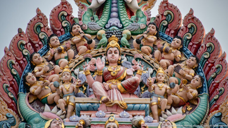 Seated goddess surrounded by many small child-like figures and flame-shaped ornament.