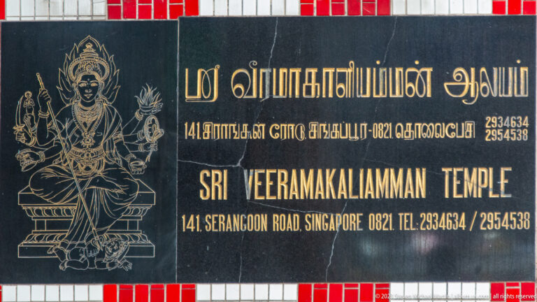 Black plaque with Tamil and English text naming Sri Veeramakaliamman Temple and its Serangoon Road address.