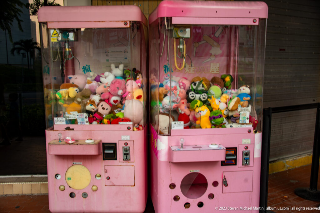 Two pink claw machines filled with colorful plush toys outside a shopfront.
