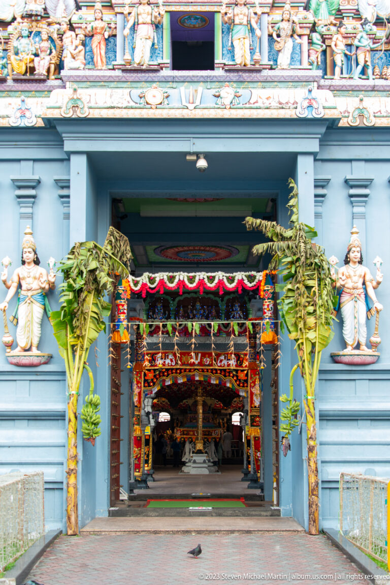 Temple entrance framed by banana trees and garlands, opening toward a decorated interior hall.
