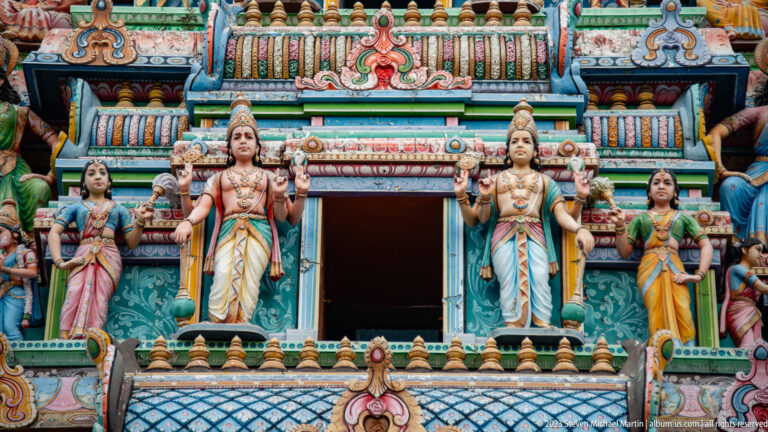 Four crowned temple figures standing around an upper doorway on a richly painted façade.