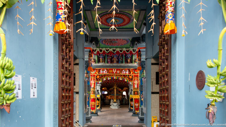 Open wooden temple doors framing a decorated passage and worship hall beyond.