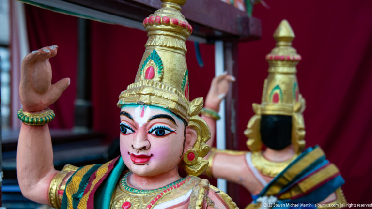 Close view of a crowned painted female temple figure with raised hands and vivid facial details.