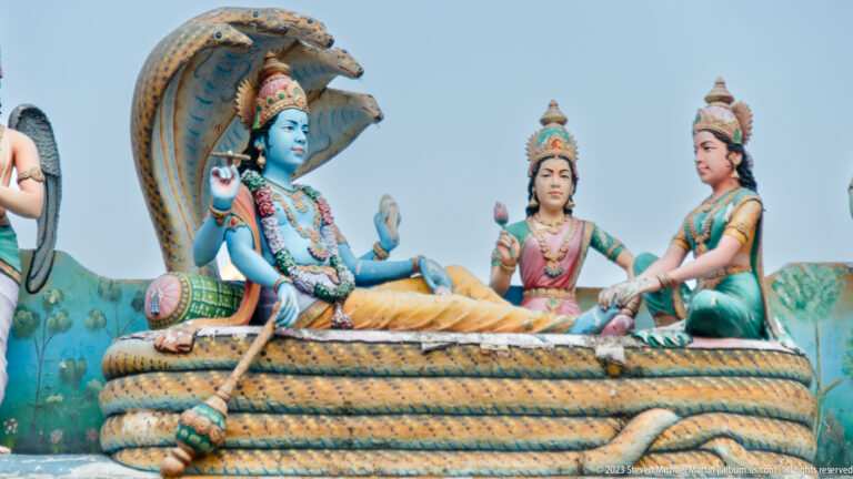 Blue-skinned Vishnu reclining on coiled Shesha beneath cobra hoods, with Lakshmi and an attendant.
