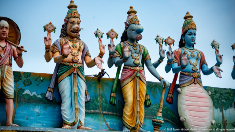 Three crowned Vaishnavite deities standing with discus, conch, and lotus-like attributes.