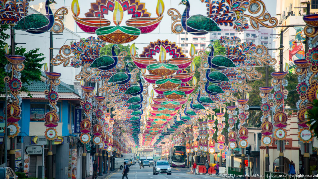 Rows of colorful peacock and lamp decorations suspended above a Little India street.