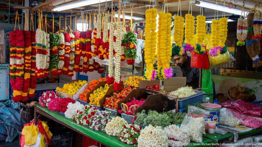 Flower stall with hanging garlands and piles of yellow, red, white, and pink blossoms.