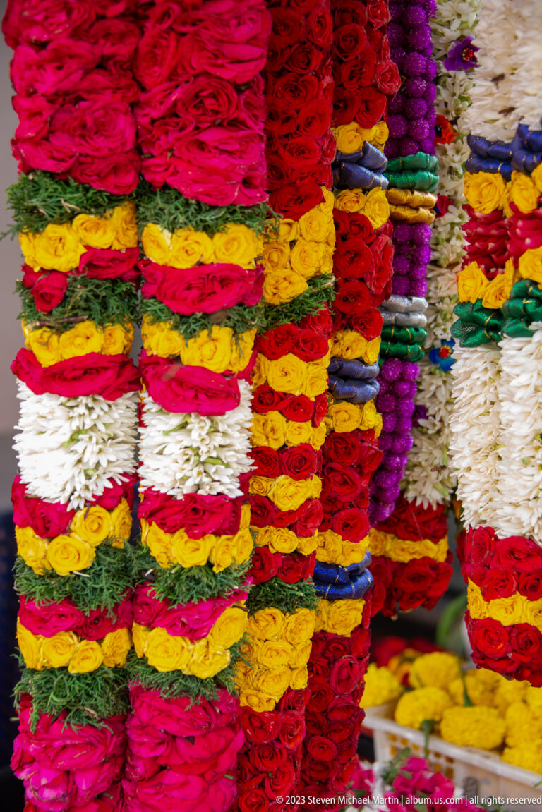 Close view of densely stacked flower garlands in red, yellow, white, pink, purple, and green.