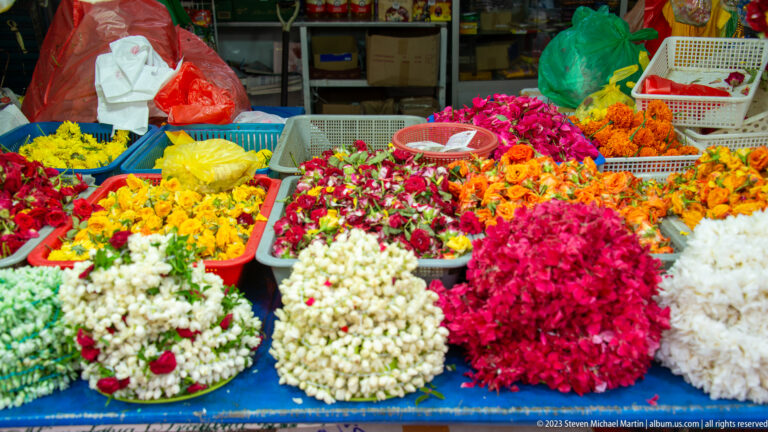 Trays of fresh white, red, pink, orange, and yellow flowers at a Little India market stall.