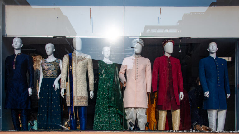 Mannequins in a shop window wearing embroidered South Asian formal garments in several colors.