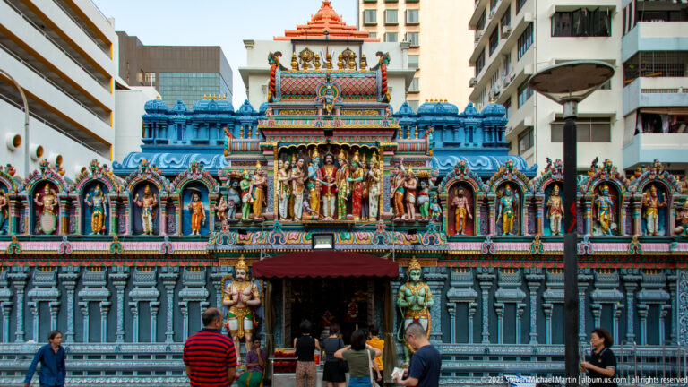 Frontal view of Sri Krishnan Temple’s blue façade with deity niches, entrance canopy, and visitors.