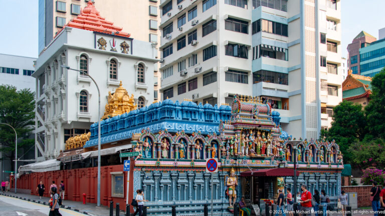 Oblique view of Sri Krishnan Temple’s blue sculpted façade beside taller modern buildings.