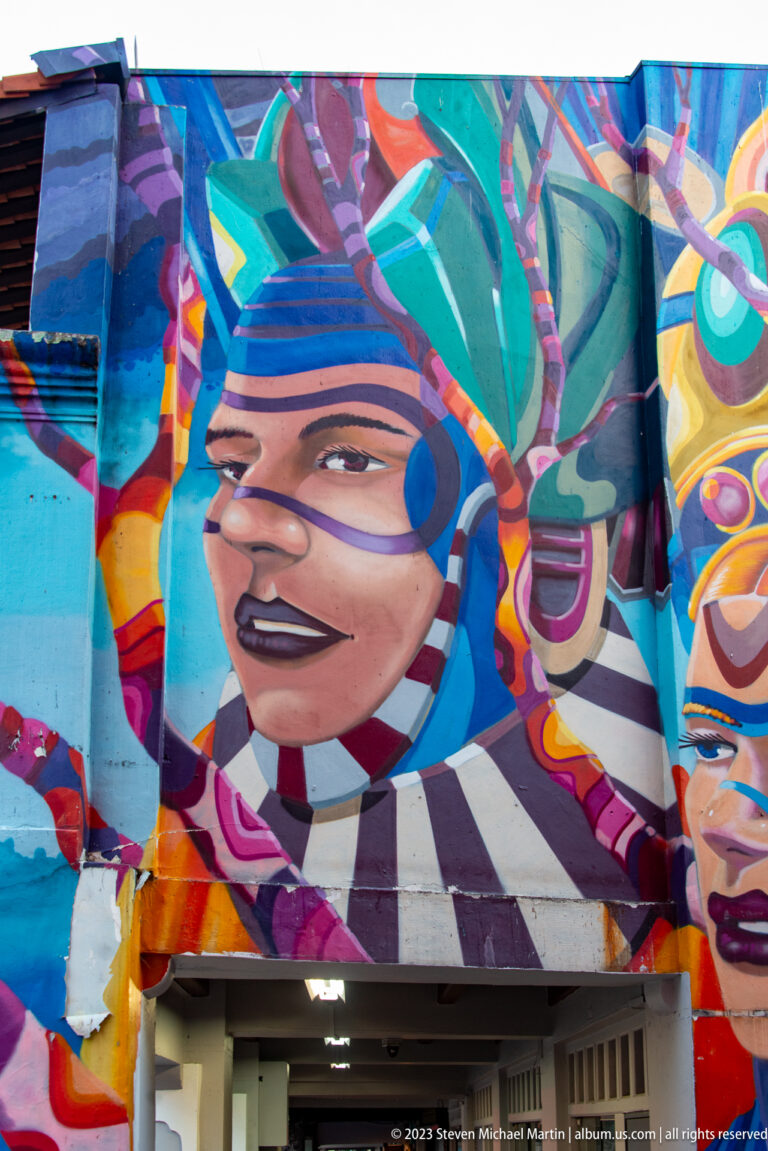 Close view of a painted face surrounded by angular blue, orange, magenta, and black mural forms.