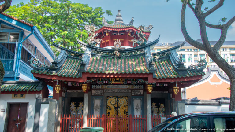 Small Chinese temple façade with green tiled roofs, red framing, painted brackets, and decorated central doors.