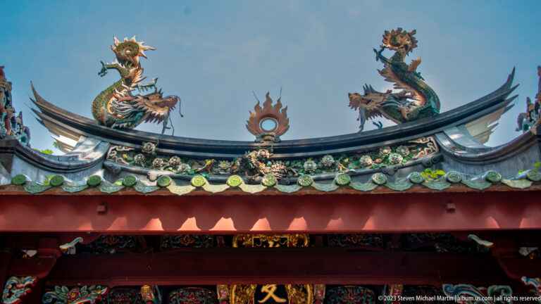 Two roof dragons face a circular central emblem above green tiles and lifted temple eaves.