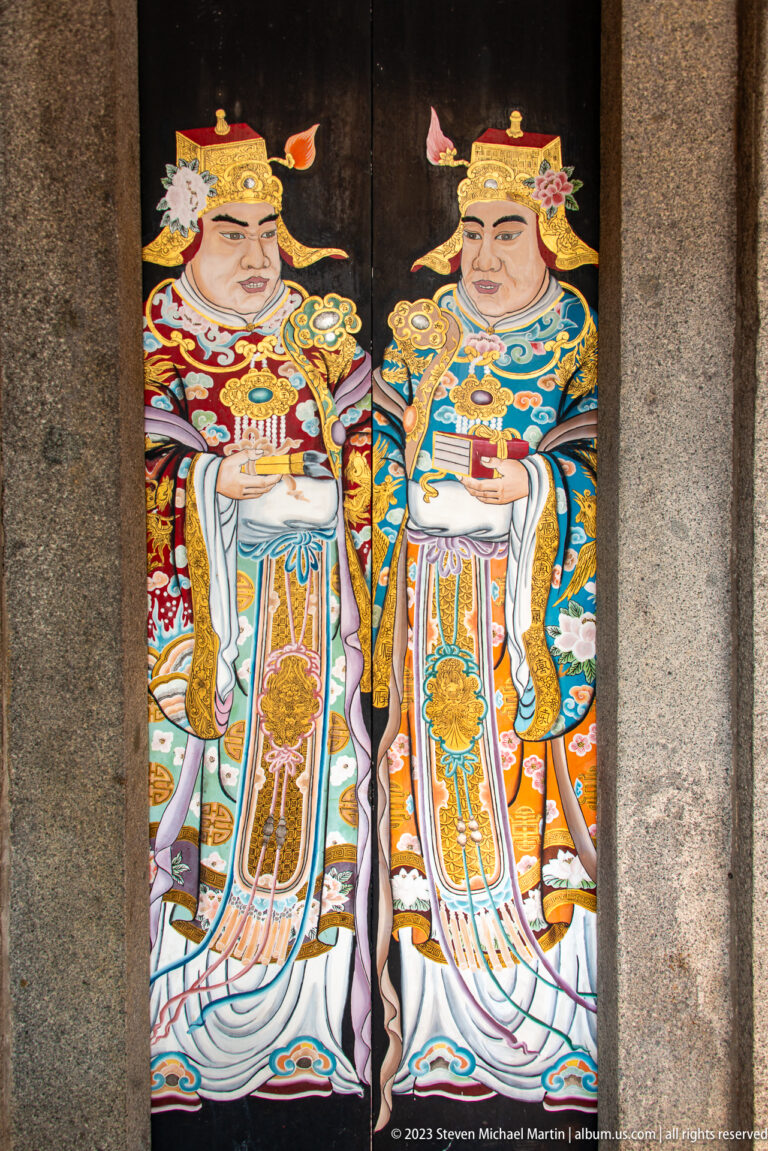 Two colorful Chinese guardian deities painted full length on adjacent dark temple doors.