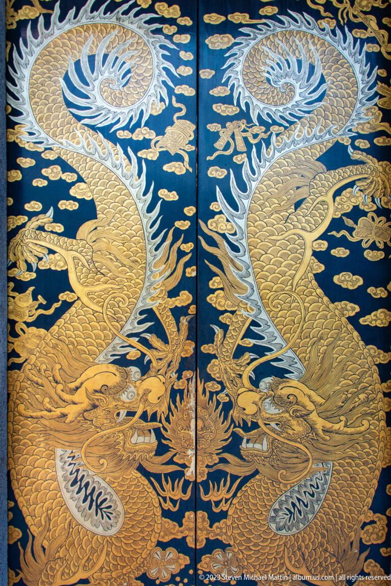 Two gilded dragons curve across dark blue temple doors amid cloud and flame motifs.