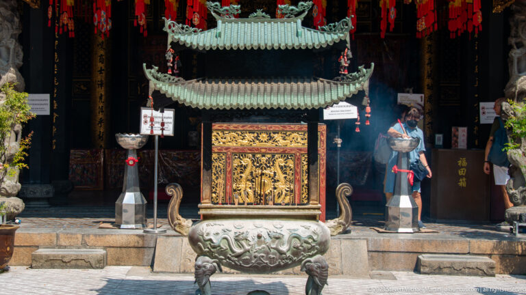 Large three-legged bronze incense burner before a tiered shrine and dark temple interior.
