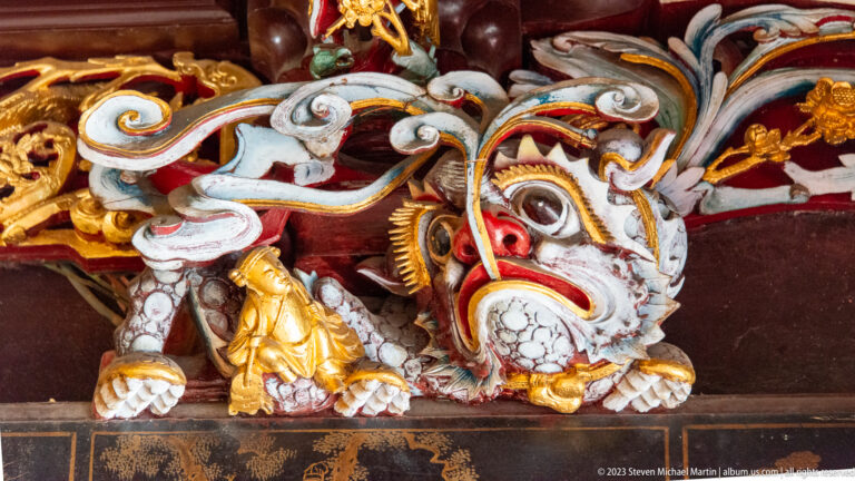 Colorful lion-like guardian carving with bulging eyes and raised paw on a wooden temple bracket.