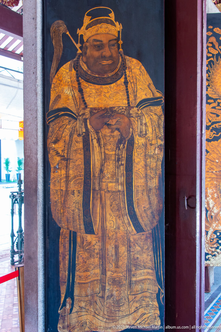 Single ochre and gold Chinese guardian deity painted on a dark temple door.