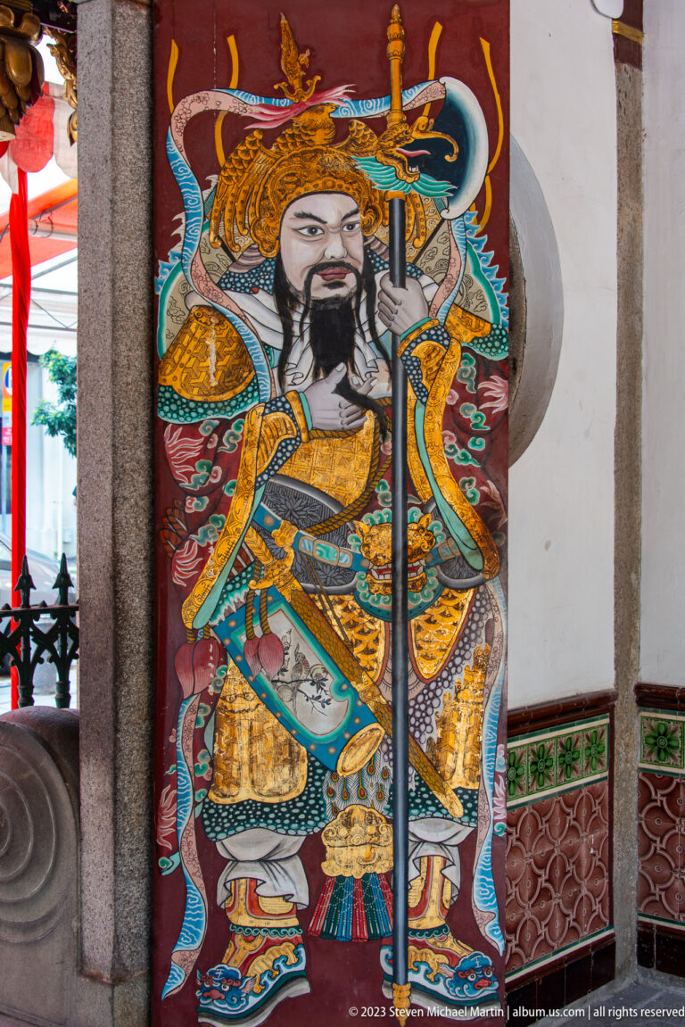 Bearded armored Chinese warrior deity holding a polearm on a brightly painted temple door.