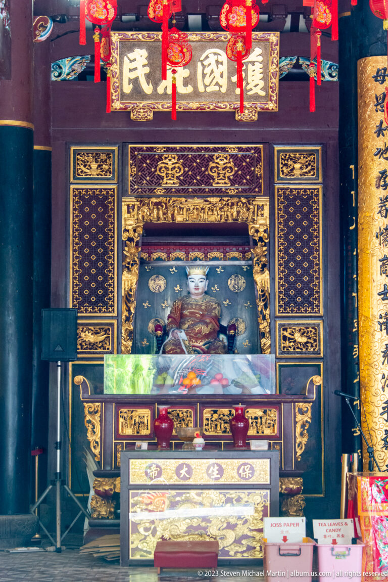 Ornate Chinese temple altar with sacred portrait, gilded carving, lanterns, and donation boxes.