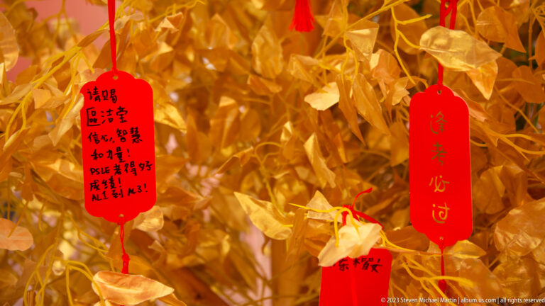 Red handwritten wish tags tied among densely folded gold-colored paper offerings.