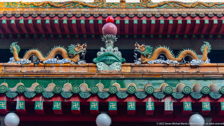 Two ceramic dragons face a central finial above green roof tiles and painted temple brackets.