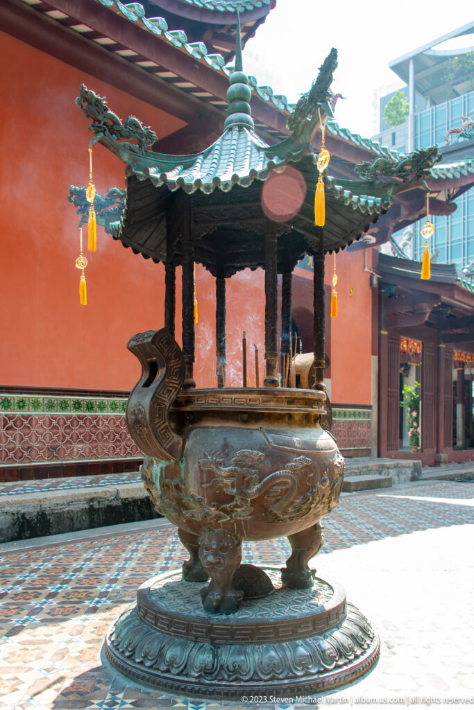 Large roofed bronze incense burner with dragon handles in a red-walled tiled courtyard.