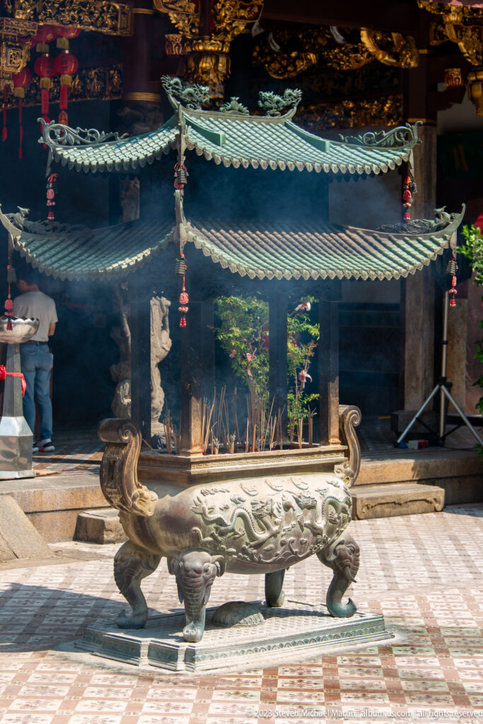 Large bronze incense burner beneath layered green-tiled canopy roofs with smoke in a temple courtyard.