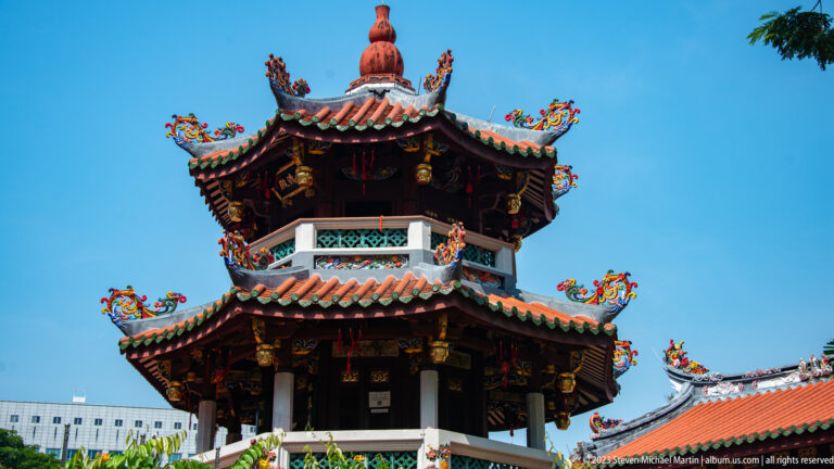 Two-tiered Chinese pavilion with red roofs, upturned eaves, dragon ornaments, and blue sky.