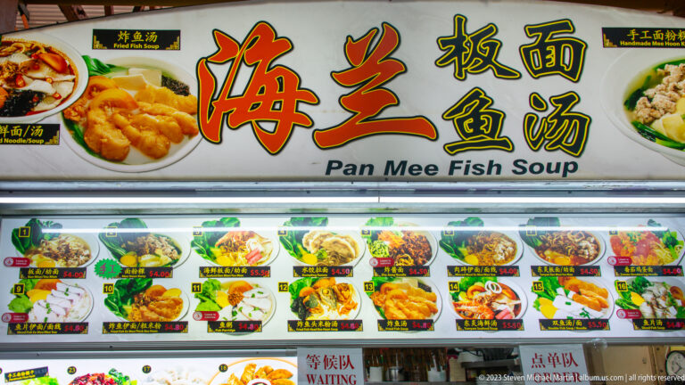 Pan Mee Fish Soup stall sign with Chinese lettering, food photographs, prices, and menu panels.