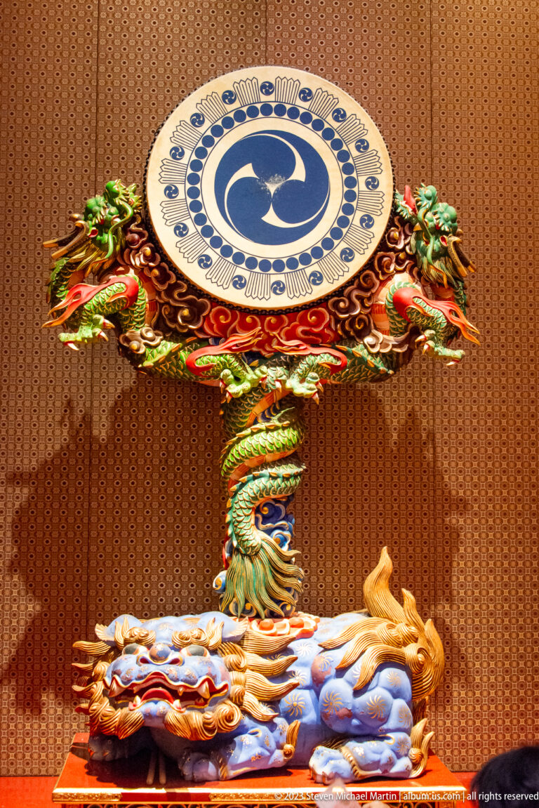 Dragon supports a circular blue-and-white emblem above a reclining figure on a cloud-like base.