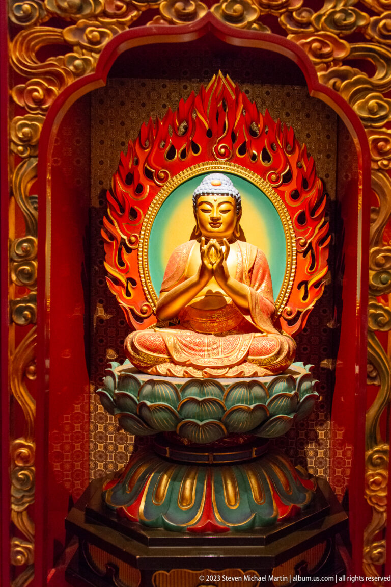 Golden seated Buddha on lotus throne beneath red flame mandorla and turquoise halo.