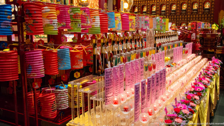 Illuminated dedication towers with paper inscriptions beneath rows of colorful hanging lanterns.