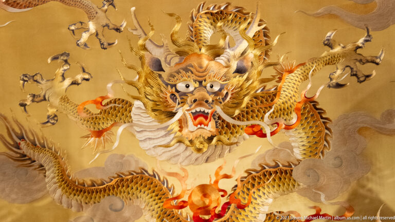 Golden dragon with open mouth and antler-like horns emerging from swirling clouds.