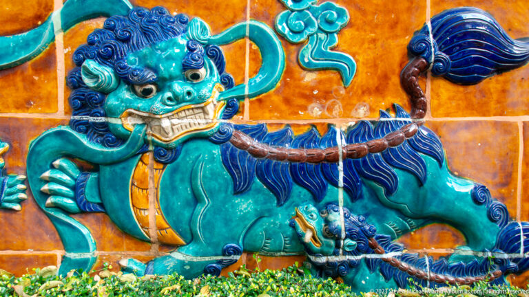 Turquoise glazed guardian lion with dark blue mane and a smaller cub against orange tiles.