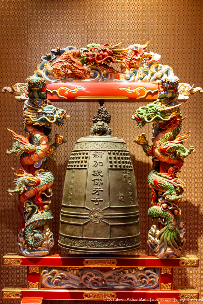 Bronze temple bell with Chinese characters framed by colorful dragons and cloud motifs.