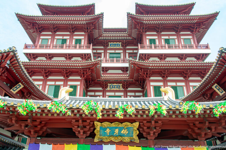 Low-angle Buddha Tooth Relic Temple façade with red-and-white tiers, projecting eaves, balconies, and gold plaque.