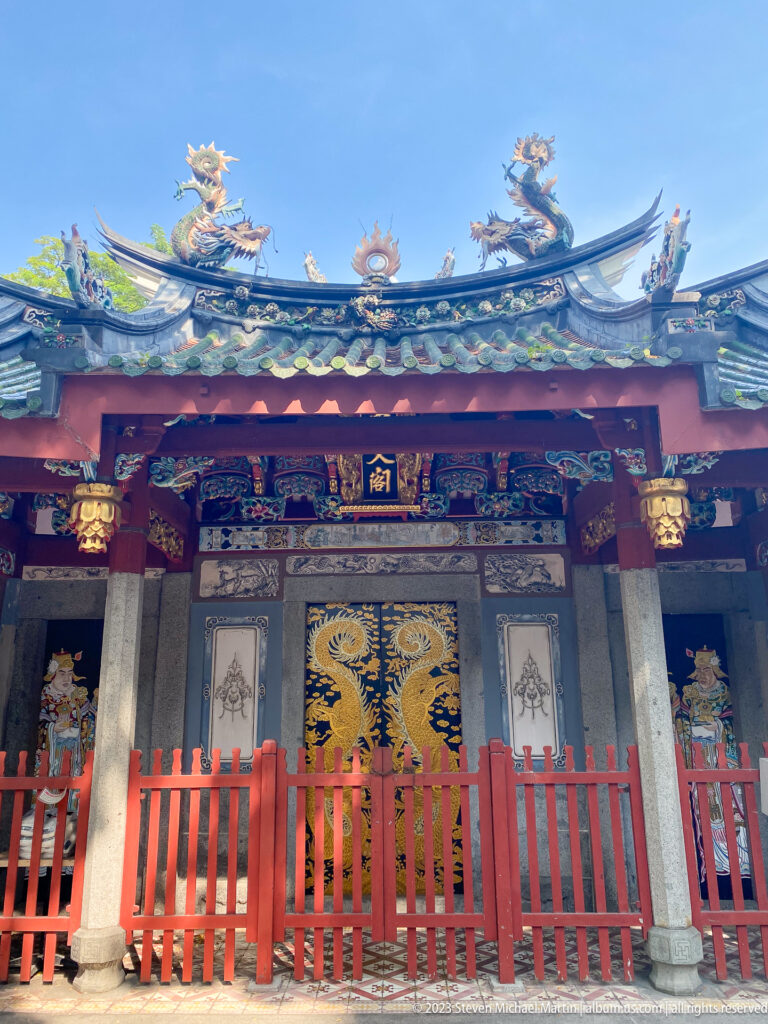 Chinese temple façade with dragon roof ridge, green tiles, red fence, stone columns, and painted doors.
