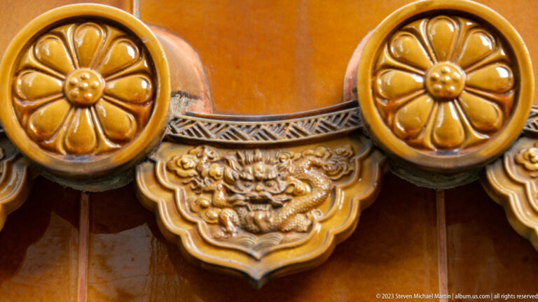 Close ochre glazed roof tile with two floral roundels and a central lion-mask relief.
