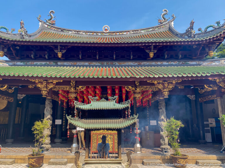 Temple hall with layered green roofs, red lanterns, and a large roofed bronze incense burner in front.