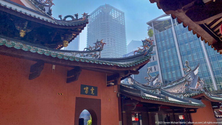 Traditional Chinese temple roofs and red wall framed by tall modern glass buildings.