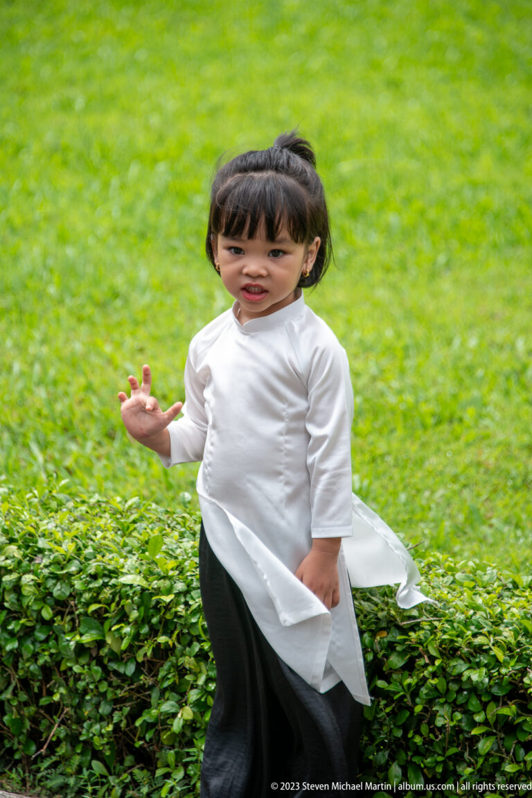 Young child in a flowing white tunic and dark trousers running across a bright green lawn.