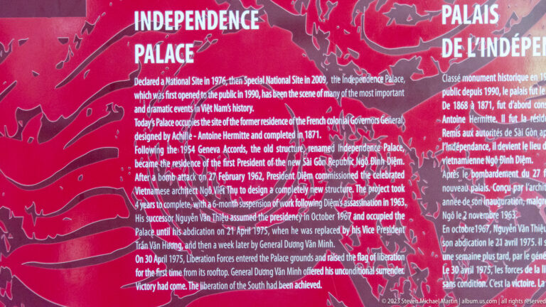 Large red multilingual wall panel explaining the history of Independence Palace in white text.