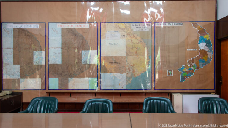 Large military maps and transparent overlays mounted behind green chairs and a conference table.