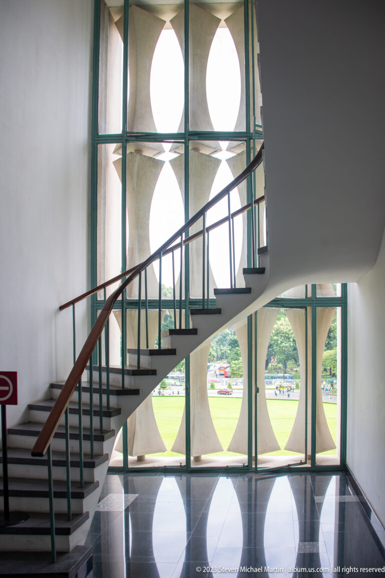 Curving white staircase beside geometric windows with turquoise frames and reflections on a polished floor.