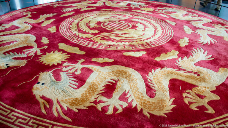 Close view of a deep red carpet decorated with two pale dragons, clouds, flowers, and a circular medallion.