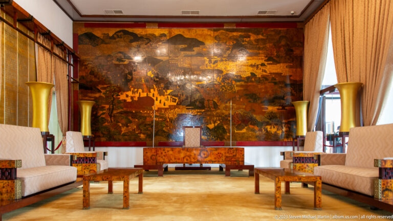 Formal hall with cream sofas, golden vases, and a large dark lacquer mural across the back wall.