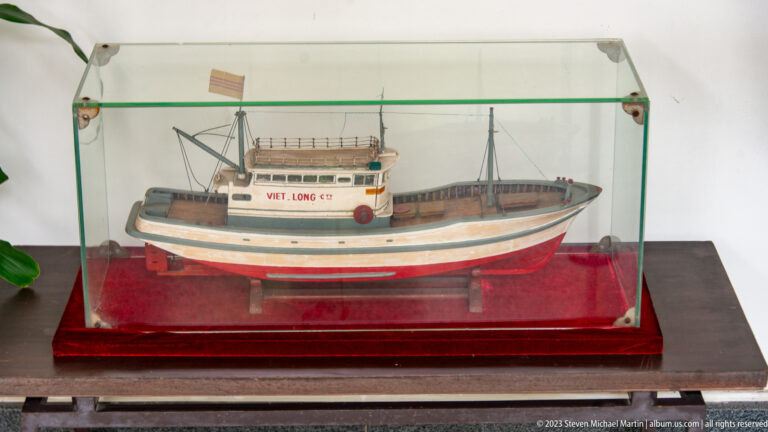 Glass-cased model of the boat VIET LONG 02 with painted hull, wheelhouse, masts, and rigging.